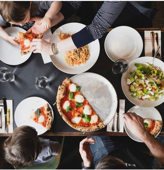 A group enjoys a meal at a restaurant with pizza, pasta, and salad shared on a table.
