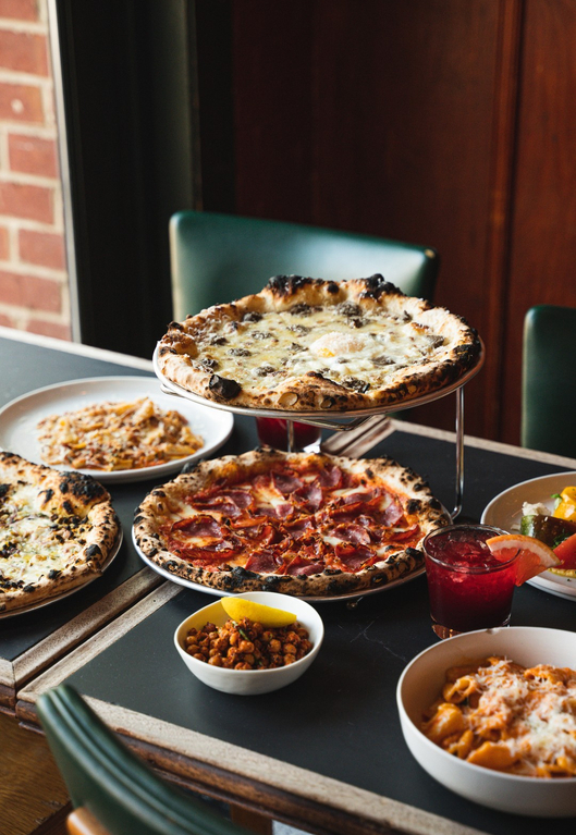Pizza set with various toppings, macaroni and cheese, and a drink served on a table in a restaurant.