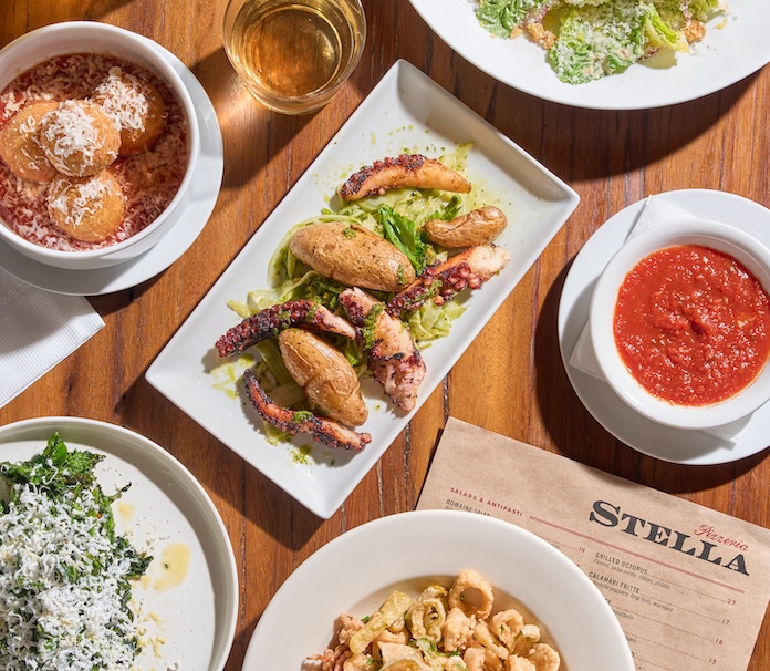 Overhead spread of Pizzeria Stella antipasti including grilled octopus, ravioli in tomato sauce, calamari fritte, and spinach with parmesan alongside the restaurant menu