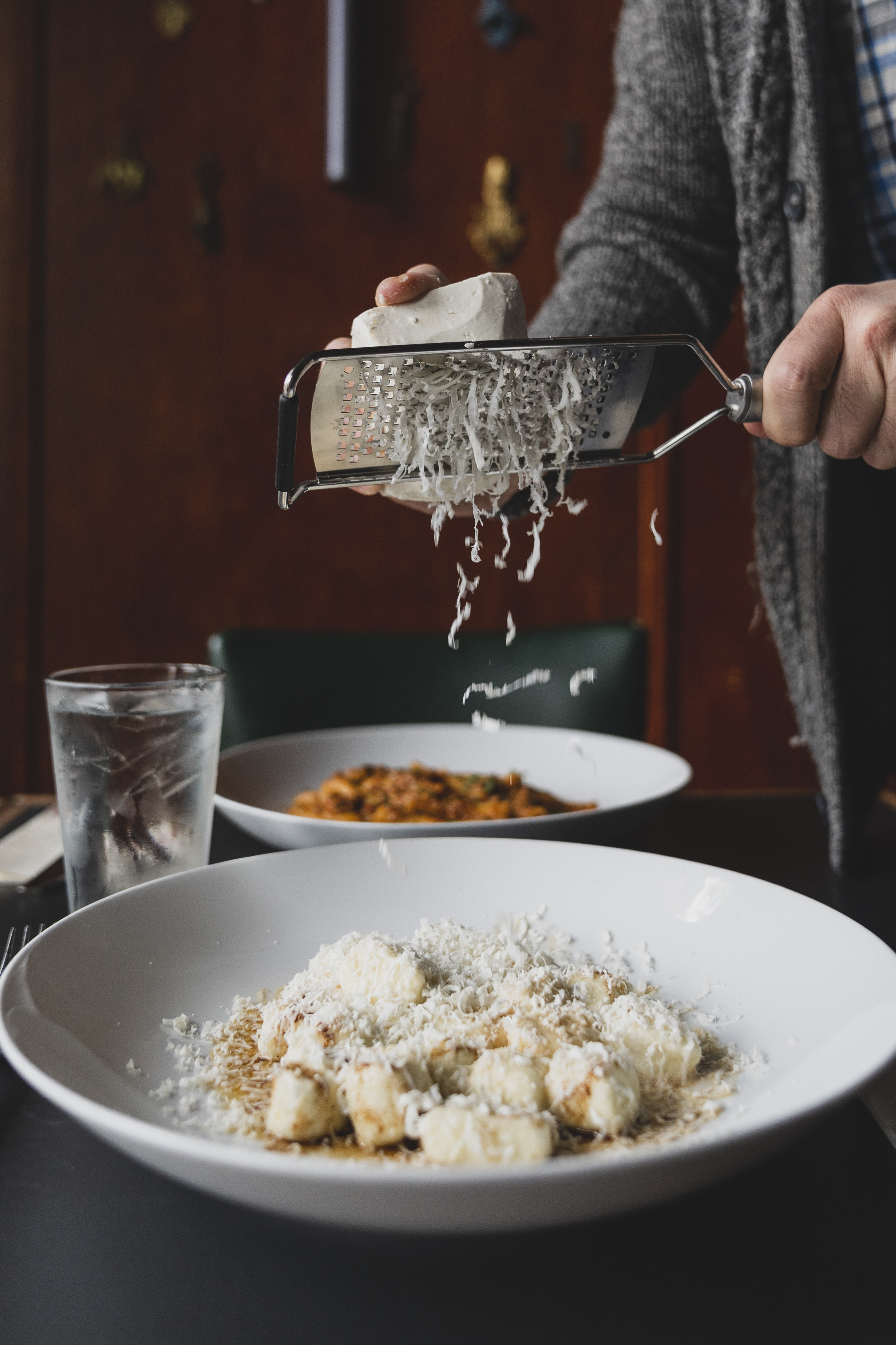 A hand grating cheese onto a bowl of gnocchi